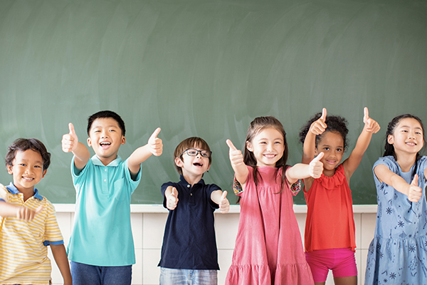 Group of smiling school children in front of a chalkboard holding their thumbs up
