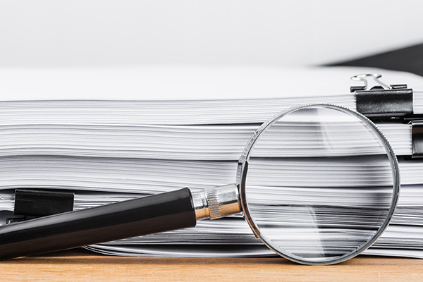 Side view of a stack of documents with a magnifying glass propped on them